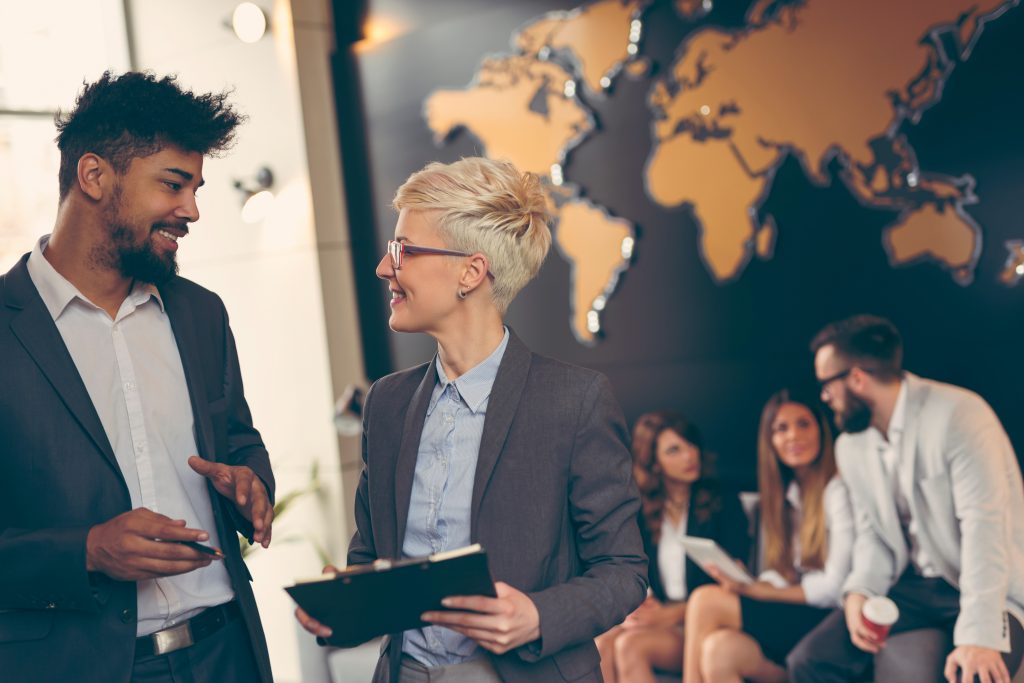 Businessman and businesswoman reviewing an international business report; business team working in the background. Focus on the man in the foreground