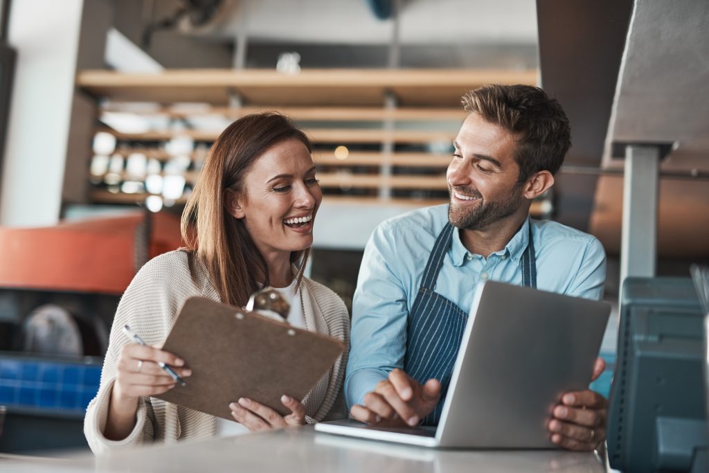 Small business, happy and couple in cafe with laptop, positive review and pride for turnover report. Restaurant owners, smile and computer at counter for information, banking and success in startup.