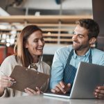 Small business, happy and couple in cafe with laptop, positive review and pride for turnover report. Restaurant owners, smile and computer at counter for information, banking and success in startup.